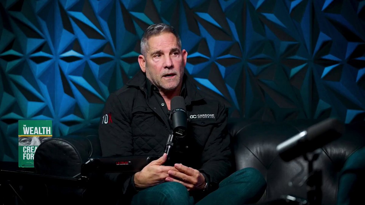 Grant Cardone is interviewed about his experience with Bitcoin in a podcast. The interview takes place in a studio setting, where he sits comfortably on a couch while talking into a microphone. The background features a blue wall adorned with geometric shapes, adding an artistic touch to the scene. The image also includes a book titled "Wealth for the Greedy" and a green hat placed nearby.