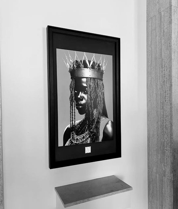 A black and white framed photograph of a woman wearing a spiked crown, displayed on a light wall above a gray shelf.