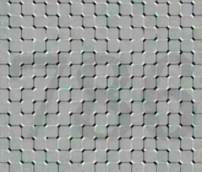 A close-up of a textured, translucent glass or plastic surface featuring a repeating pattern of interlocking square grid shapes.