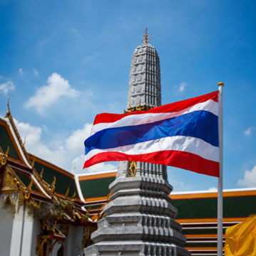 The Thai flag waves proudly in the foreground against the backdrop of an ornate Buddhist temple spire and traditional roof architecture, symbolizing Thailand's cultural heritage. This iconic imagery complements the news of Thailand's official confirmation of a 0% capital gains tax on Bitcoin and crypto trades, positioning the country as an emerging digital asset hub.