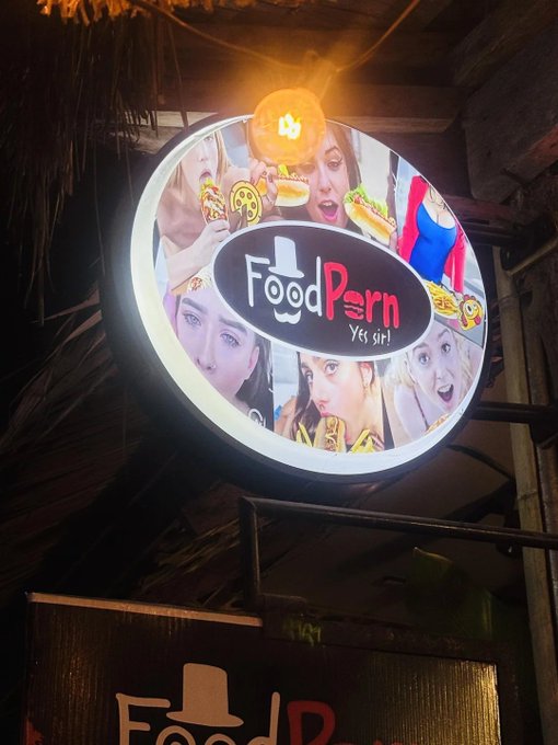 An illuminated circular sign for 'FoodPorn' restaurant, featuring the tagline 'Yes, sir!' and images of people eating burgers and hot dogs.