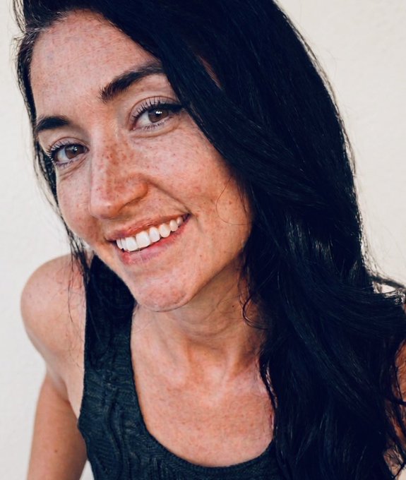 A smiling young woman with long dark hair and freckles, wearing a gray tank top, radiates positive energy that perfectly matches the upbeat "GM" (Good Morning) message wishing the $XRP community a happy Thursday. Her bright, genuine smile embodies the positive vibes the post is encouraging its readers to share in return.