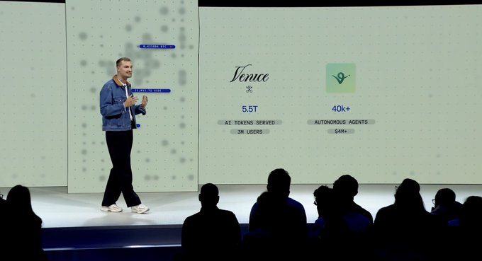 The image shows a man standing on stage, giving a speech or presentation. He appears to be wearing a blue jacket and black pants. The audience consists of several people sitting behind him, attentively listening to his words. In front of the speaker, there is a screen displaying information about a cryptocurrency called @base + @coinbase. This indicates that the event might be related to the world of finance or technology, possibly discussing the future of digital currency and its impact on society.