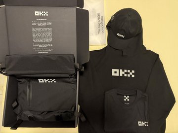 An unboxing of OKX branded merchandise including a hoodie, cap, and pouch set against the branded packaging.