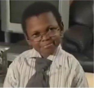 A young boy wearing glasses, a striped dress shirt, and a tie, giving a slight smirk in what appears to be an office setting.
