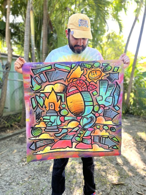 A bearded man wearing a tan "Miami Dolphins" cap holds up a vibrant, psychedelic graffiti-style painting featuring abstract shapes, a smiling sun, hearts, and bold colors, fitting the "Miami graffiti Solbot" theme of the post.