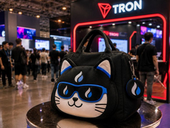 The image features a black cat-themed purse displayed on top of a table, with a bull cat design on it. The purse has blue sunglasses attached to it, giving it a cool and stylish appearance. In the background, there are people walking around in front of a booth that says "TRON" on it. This suggests that the purse might be related to the cryptocurrency world or could be a promotional item for a gaming event where tron is being showcased as a popular game mode. The post about the bull cat mode also seems to be connected to this scene, possibly promoting a new mode in the game or highlighting a specific feature of the purse design.