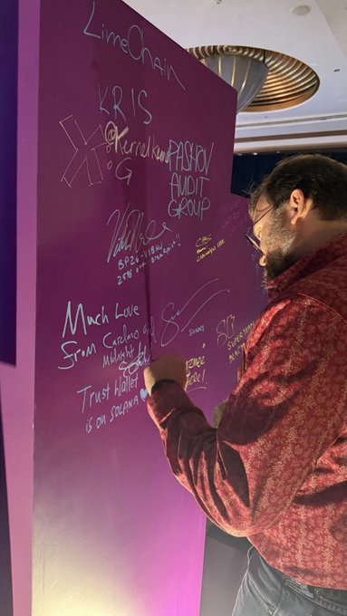 A man signs a purple wall covered in messages from LimeChain, KRIS, and Passion Audit Group, including "Much Love from Carolina... Trust bilder... is on Solana," with "Peace" added at the bottom—capturing the celebratory send-off mood of "until next time."