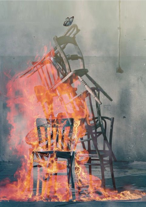 The image shows a fire burning brightly against an unusual background, casting flames over several black chairs. The chair closest to the viewer appears to be on fire. The remaining chairs are situated at various distances from the center of this blaze, with one chair positioned right in front and others located further back. A person can be seen standing near the center of the image, seemingly observing or taking part in the unfolding scene. In the corner of the photo, there is a caption that reads "Hope Until the Very Last Moment Gm 1/1." This message might relate to the dramatic nature of the fire and the intense moment captured within the image.