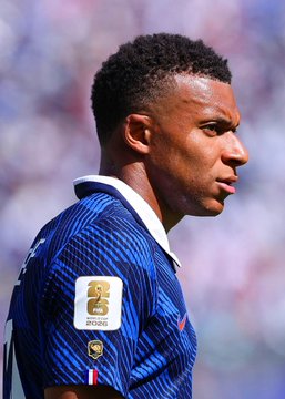 A close-up side profile of French footballer Mbappé wearing the blue and white French national team jersey with the FIFA World Cup 2026 patch is shown. The image relates to the post by depicting the French team key player, whose performance will be pivotal in the match against Spain where a $5M bet has been placed against France winning.