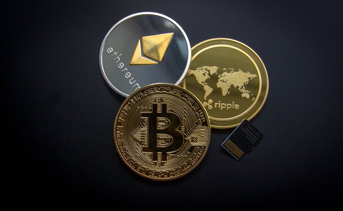 Three physical representations of major cryptocurrencies—Ethereum, Bitcoin, and Ripple (XRP)—along with a microSD card, sit arranged on a dark surface. The image visually reinforces the article's point about the vast crypto ecosystem, contrasting the massive adoption of these digital assets with the tiny number of ultra-wealthy holders who control the bulk of the wealth.
