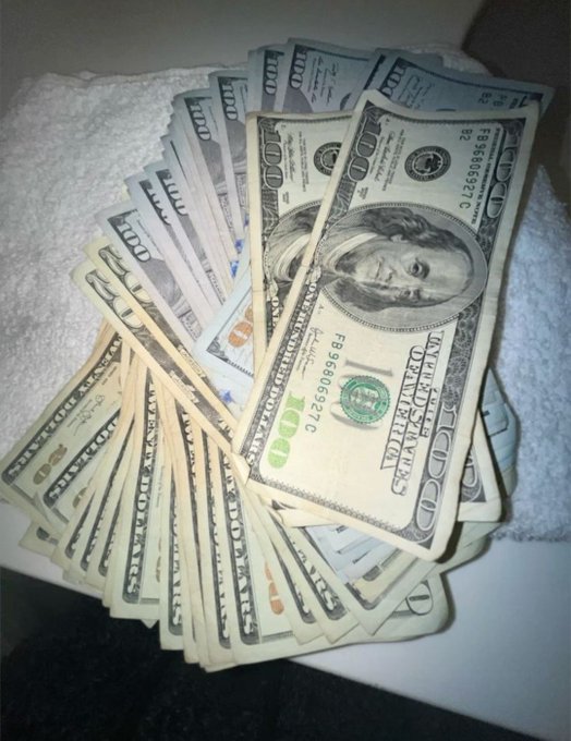 A fan of U.S. $100 bills, including several with serial number FB96666927C, is spread out on a white towel. The cash display visually reinforces the caption's motivational message about making money.