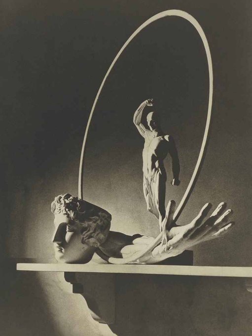A black-and-white photograph captures a sculpture of an athlete leaping through a ring, standing triumphantly atop a fallen figure.