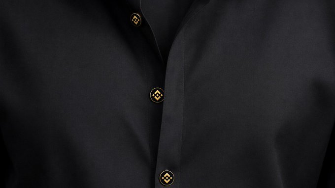 Close-up of a black shirt featuring gold circular buttons with a geometric logo design.