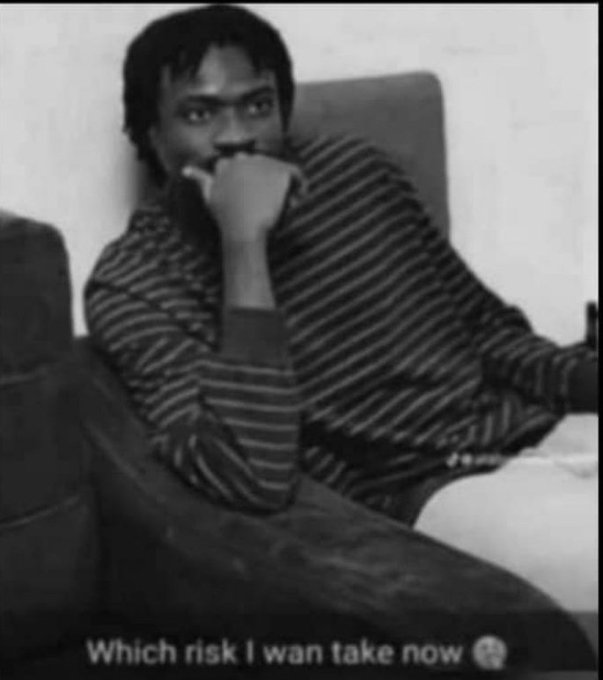 A black-and-white photo of a man in a striped sweater sitting thoughtfully with his hand over his mouth, captioned "Which risk I wan take now."