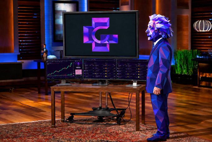 A low-poly 3D-rendered figure in a blue suit and bearded mask stands before a multi-monitor trading setup, gazing at a central screen displaying a purple geometric "G" logo, evoking the polished aesthetic of a pitch-ready product reveal. The scene visually reinforces the post's message about launching a major new consumer crypto app on BNB Chain, positioning Genius.fun as a sleek, user-friendly gateway to onchain opportunities.