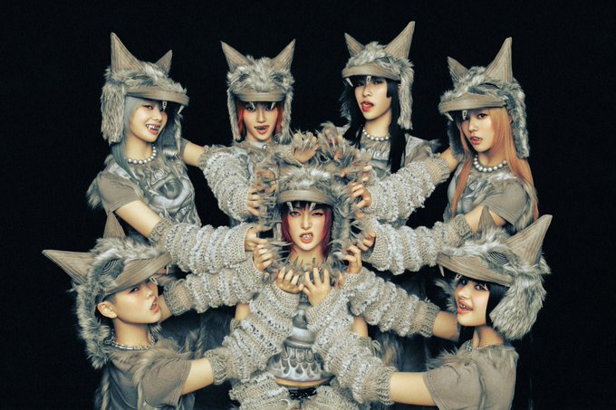 A group of women in elaborate gray furry hats with pointed ears pose dramatically together in a dark setting, with one woman at the center baring fangs.