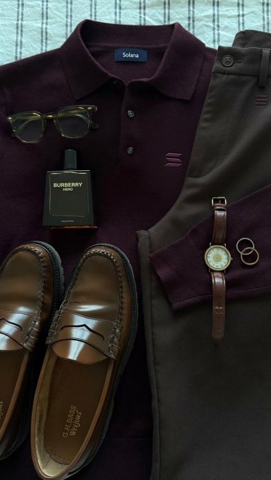 A flat lay of men's fashion items featuring a burgundy Solaro polo shirt, olive trousers, G.H. Bass loafers, a Burberry Hero cologne bottle, sunglasses, a wristwatch, and a ring.