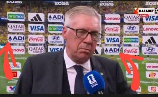 An interview with an older man in glasses and a suit speaking into a DAZN microphone, with World Cup sponsor logos behind him and red arrows drawn pointing to certain brands.