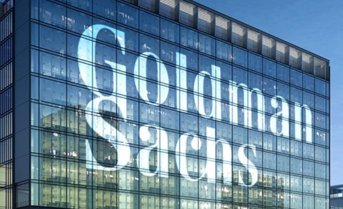 The image shows a modern glass office building with the "Goldman Sachs" logo prominently displayed on its facade. It visually represents the financial giant at the center of the reported $2.25 billion acquisition of NEOS Investments, signaling its expansion into cryptocurrency.