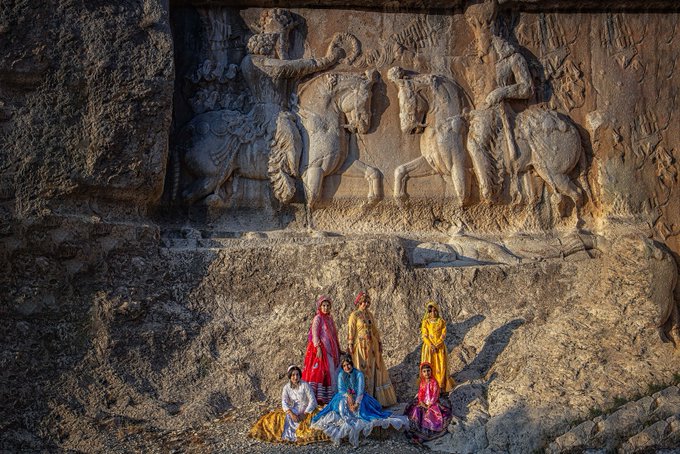 Same image as Image 2: women in colorful saris pose beneath an ancient rock relief carving of mounted horsemen.
