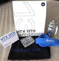A promotional merchandise set from HTX's 13th Anniversary, featuring a white box, metal water bottle, black cap, and branded card reading "HTX 13TH ANNIVERSARY" and "ONLY ON HTX".