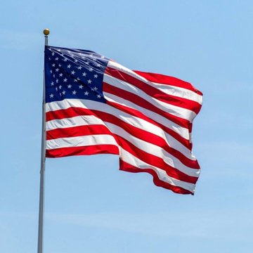 An American flag waves against a clear blue sky, symbolizing the United States as a federal judge temporarily blocks Minnesota's ban on prediction markets, citing federal preemption.