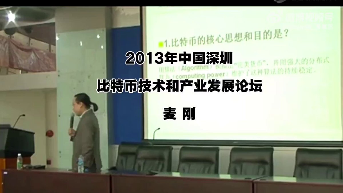 The image shows a man standing at a podium, giving a presentation or lecture. The room has a large screen behind him displaying information related to cryptocurrency. The text "2013" can be seen in the image as well. This suggests that the event might be taking place on a specific date, possibly during the year 2013.