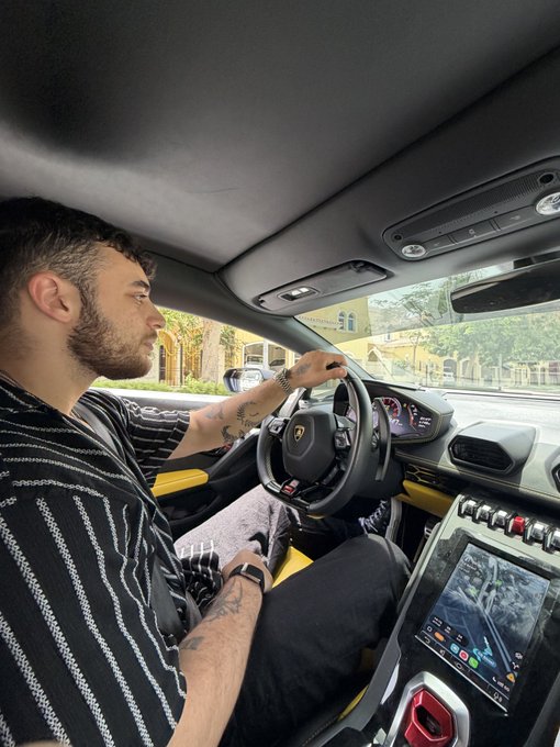A bearded man sits behind the wheel of a Lamborghini, his tattooed arm extended across the steering wheel, with the car's digital dashboard and infotainment screen visible in the cabin.

The "GM" caption likely refers to the "General Motors" abbreviation or possibly a personal handle, though the luxury Italian sports car in the image contrasts with American automaker branding—suggesting the post may be highlighting the driver's experience or promoting a premium lifestyle tied to that moniker.