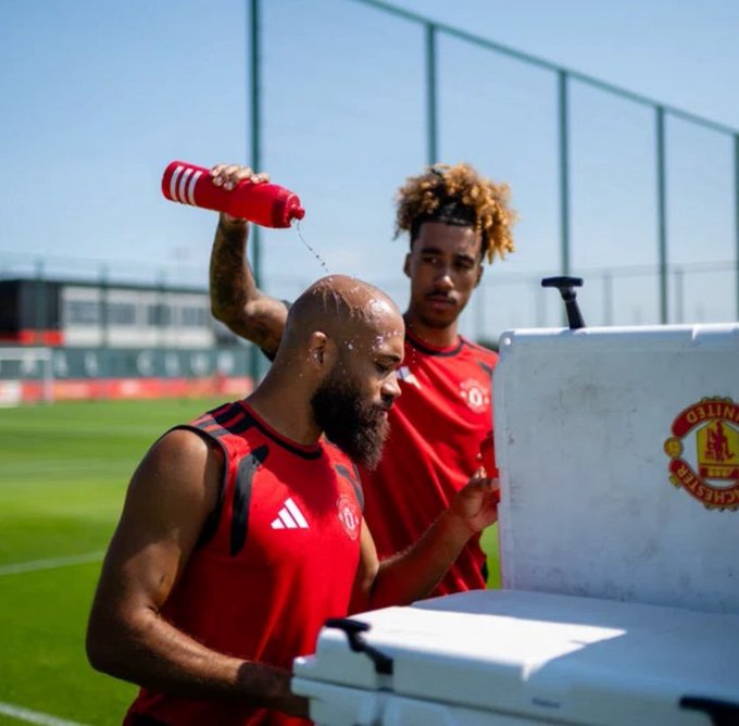 A Manchester United player pours water over his bearded teammate's head during a sunny training session, with the Manchester United crest visible on a nearby cooler, illustrating a lighthearted "comforting" gesture that contrasts ironically with the post's dark humor about financial loss.

Alternative version:

Two Manchester United players in red training gear share a light moment at training, with one pouring water over the other's head near a cooler bearing the club crest—a jovial scene that provides ironic visual contrast to the post's morbid joke about losing money on a failed meme coin investment.