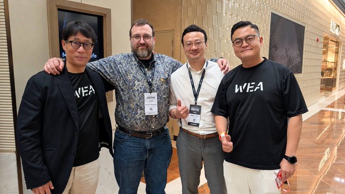 Four men pose together at what appears to be the TOKEN2049 conference, with two wearing matching black "WEA" branded t-shirts. The post contextualizes the photo as a moment following WEA's stablecoin payments demo on merchant rails powered by NetX, highlighting the practical architecture behind real-world crypto adoption rather than just promotional messaging.