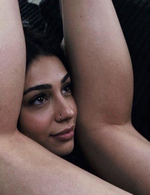 A woman with dark hair and a nose ring rests her head between her raised arms in an intimate, sensual pose. The relaxed, carefree posture contrasts with the post's motivational message about taking control of life through disciplined investing, suggesting that true "rawdogging" of life means achieving the freedom to enjoy quiet, intimate moments rather than letting financial pressures dominate you.