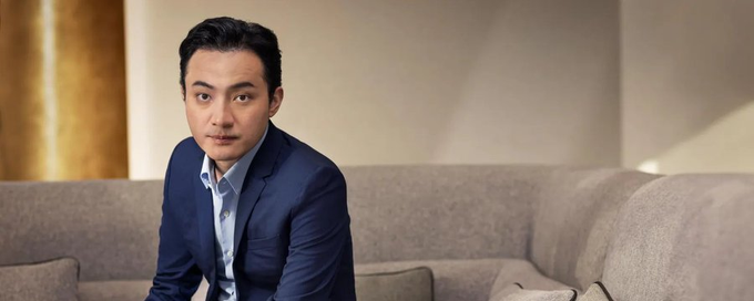 A man in a navy blue suit sits on a gray sofa looking directly at the camera, appearing serious and composed. Based on the accompanying article about a federal judge rejecting World Liberty Financial's bid to move Justin Sun's claims to arbitration, the image likely depicts Justin Sun, the TRON founder involved in this legal dispute.