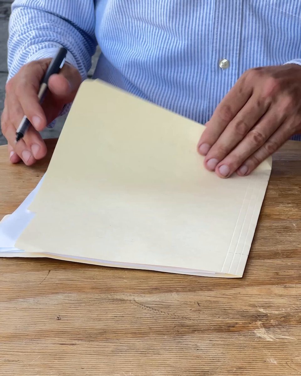 The image shows a person sitting at a wooden table, writing with a pen on a piece of paper. The scene takes place outdoors, possibly during sunset or early morning hours when natural light is more prominent. The text "troy is one of the few good things that still exists in the bitcoin ecosystem" appears to be related to the image and the post about Bitcoin.