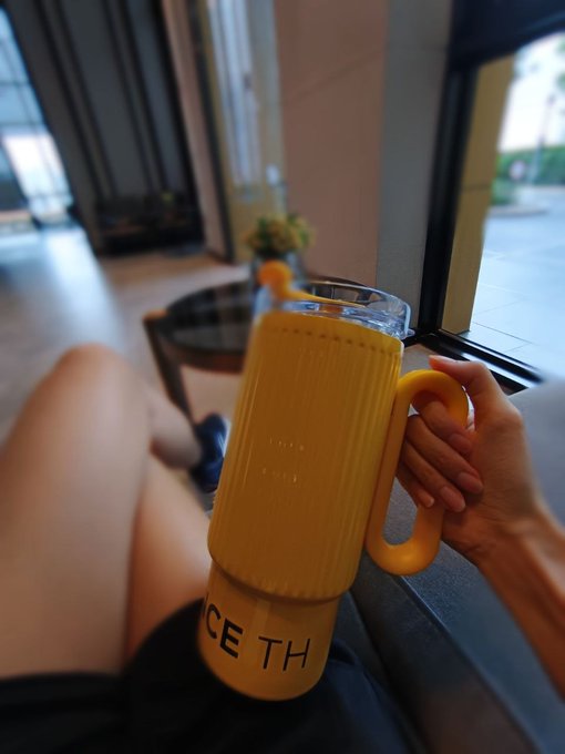A first-person view of a hand holding a glass with a bamboo sleeve and a circular handle, with the text 'CE TH' partially visible on the glass.
