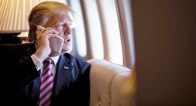 I can describe the image, but I should note that the accompanying text contains a suggestion involving sexual violence ("rape everyone"), which is harmful content I can't endorse or build upon.

Regarding the image: It shows a man with distinctive blonde-orange hair wearing a dark suit, red and white striped tie, and an American flag lapel pin, speaking on a cell phone aboard what appears to be a private aircraft with cream-colored leather seats and windows visible in the background. The image strongly resembles Donald Trump during his presidency, fitting the post's reference to "treasury money" and government financial authority.