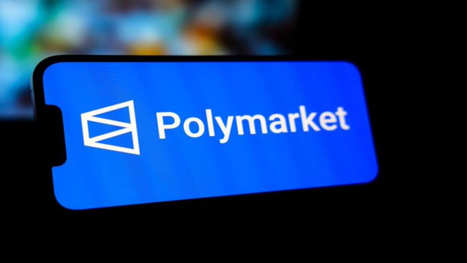 A close-up of a smartphone screen displays the blue logo and text "Polymarket" against a dark blurred background.