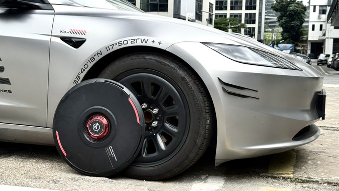 Photo of a silver sports car parked outdoors with coordinates '33°40'18"N 117°50'21"W' marked on the fender, alongside a Hub-style wheel center cap leaning against the tire.