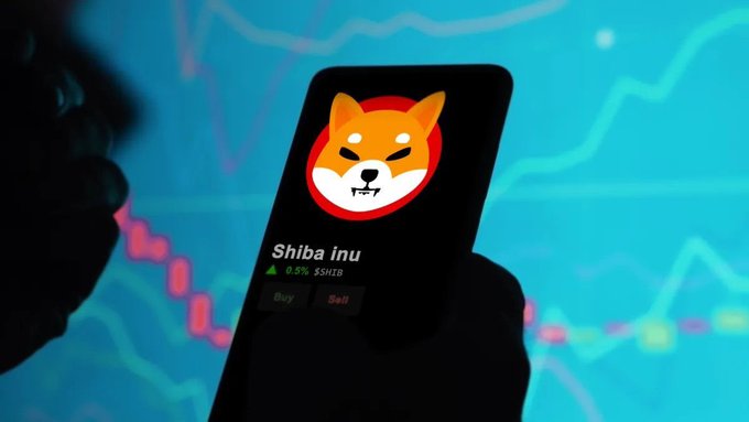 A hand holds a smartphone displaying the Shiba Inu (SHIB) cryptocurrency logo and a buy/sell interface, set against a blurred background of a blue stock chart.