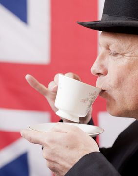An elderly gentleman in a top hat sips tea from a delicate floral cup and saucer, with the Union Jack flag serving as the backdrop—evoking a quintessentially British scene that ties into the story of a British man's improbable recovery of long-lost Bitcoin holdings.