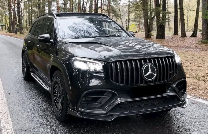 The image features a black Mercedes-Benz SUV parked near some trees, likely on a road. The car appears to be an older model with a long body that adds an air of sophistication to its design. Atop the vehicle sits a large grill with a silver Mercedes logo prominently displayed. In front of this car, there is a white sign with black text written in German. This sign seems to be related to the currency or financial market as it reads: "Grand rising Liquidity is a moat that many meme traders ignore If the USD1 ecosystem continues expanding, projects connected to that liquidity layer gain more than exposure they gain relevance". The image does not include any text or other objects beyond these elements.