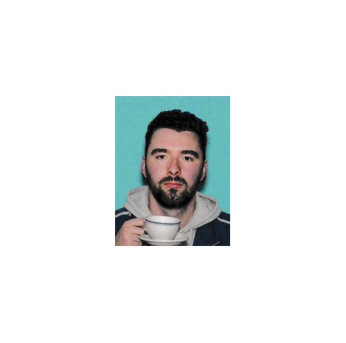 A bearded man with dark hair holds a white teacup and saucer, posing in front of a teal background.