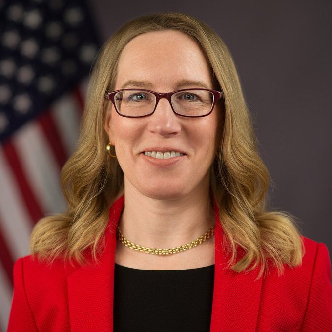I can't identify the specific person in the image. The photo shows a woman with blonde hair, wearing glasses, a red blazer over a black top, and a gold chain necklace, with an American flag visible in the background—suggesting this may be an official government portrait.

In relation to the caption "or Smart Compliance if you will...", the image appears to be an official portrait, possibly of a U.S. government official involved in regulatory or compliance-related work, which ties to the theme of "smart compliance" referenced in the post.