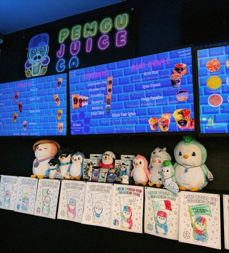 A neon "PENGU JUICE CO" sign illuminates a brick-patterned menu board above a shelf lined with Lil Pudgy penguin plushies, figurines, and hand-drawn fan artwork celebrating the Pudgy Penguins community IP, with one large mascot penguin highlighted as "Luke," created by @theweb3attorney.