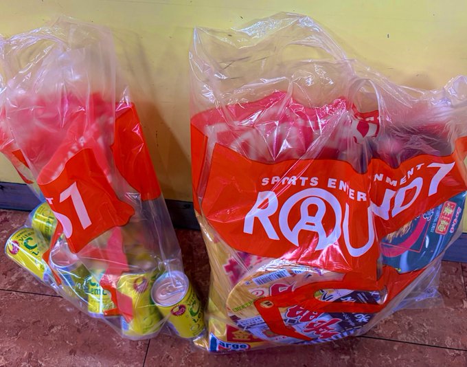 The image shows a bag of sports equipment, including cans of soda, placed next to another bag filled with sports equipment. The bags are sitting on a tiled floor, possibly at an event or gathering where people have brought their own refreshments for everyone to enjoy during breaks in games and activities.