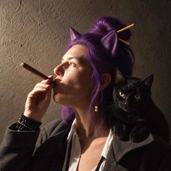 A person with vibrant purple hair styled in a bun with wooden sticks smokes a cigar, while a black cat perches on their shoulder against a dark gray background.