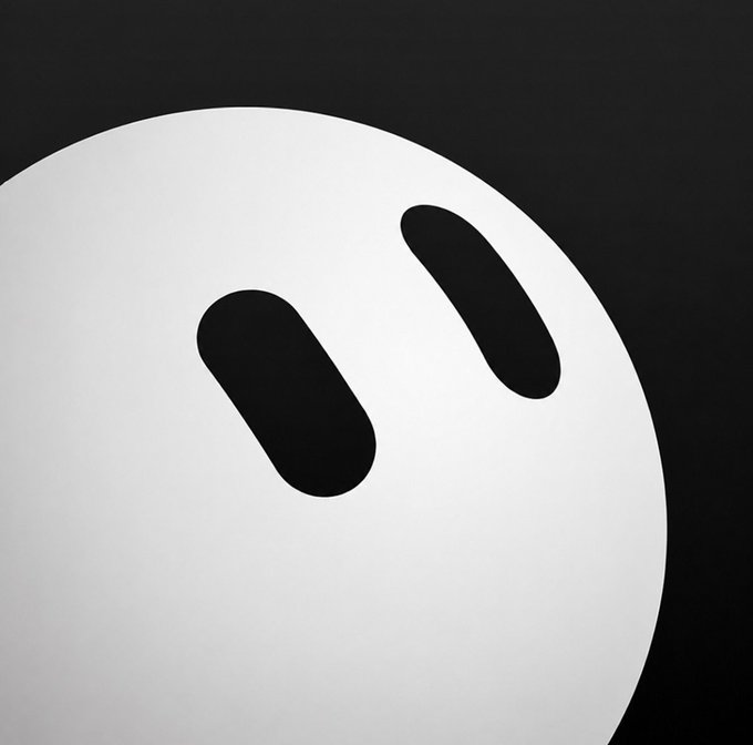 A close-up of a minimalist gray face design with two oval black eyes on a dark background.