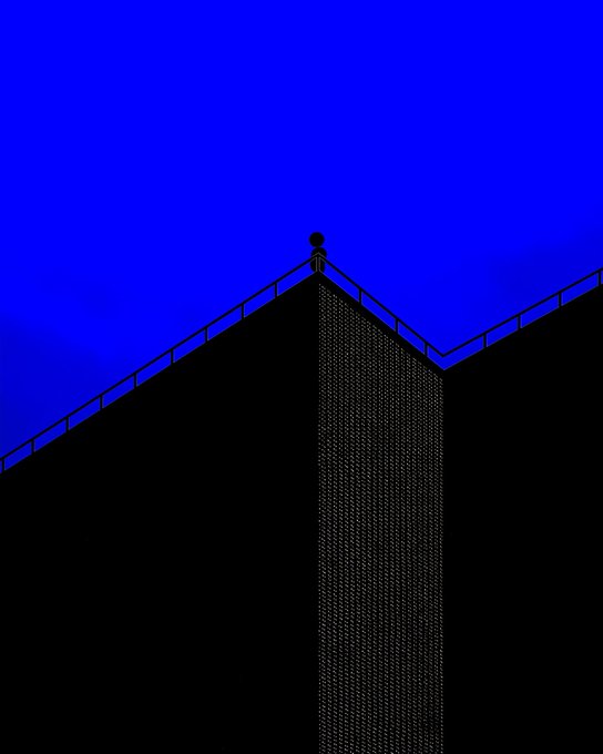The image features a tall building with a balcony at the top of its structure. The sky above the building has a blue hue, creating an interesting contrast between the man-made architecture and the natural environment. The photo appears to be taken from below, looking up towards the building, which adds depth and perspective to the scene.