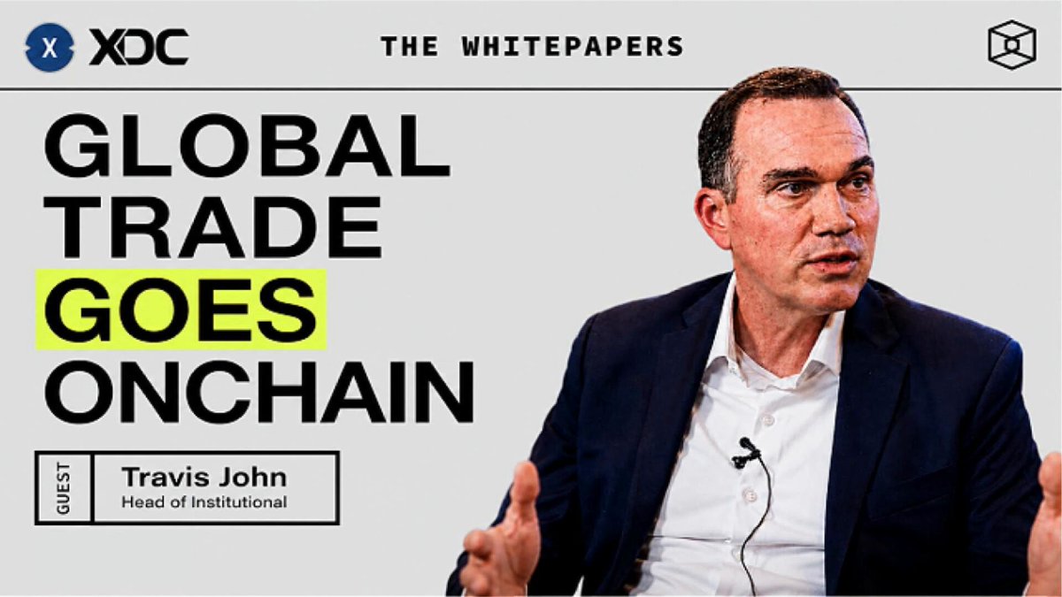 The image features a man wearing a suit, sitting down with his hands together as he speaks into a microphone. The background of the image is white, making him stand out against it. There are also some text elements present in the image that read "Global Trade Goes Onchain" and "The White Papers". This suggests that the image might be related to a presentation or discussion about global trade and blockchain technology.