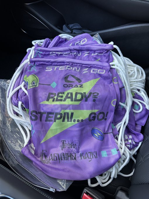 Purple 'STEP N GO! READY?' drawstring bags with white ropes piled in what appears to be a car seat, featuring text 'From MABANDI KIDS' and other graphic designs.